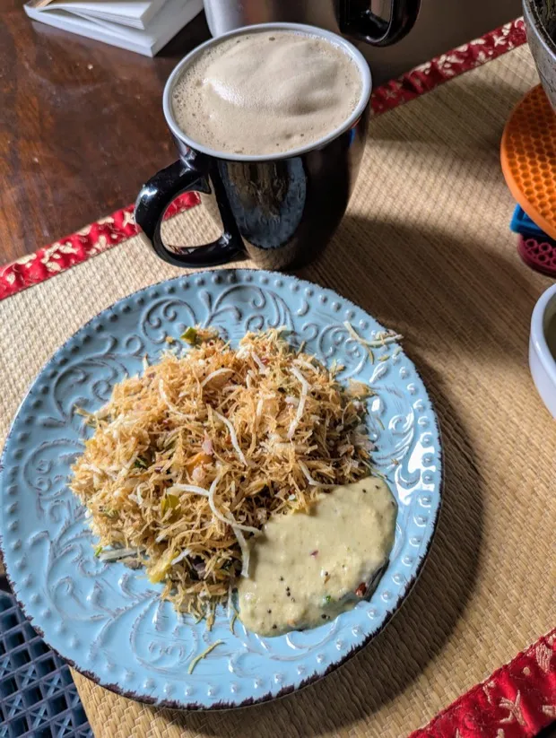 Vermicelli upma topped with shredded coconut and fine sev on a blue plate, with coconut chutney and a mug of filter coffee