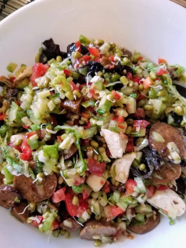 A large bowl of chopped salad with sprouted mung, tomato, cucumber, celery, olives and mushrooms